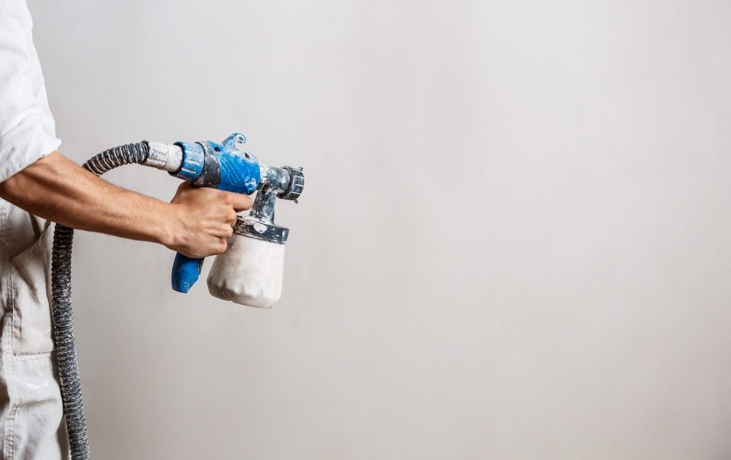 Worker painting wall with spray gun in white color. Copy space.